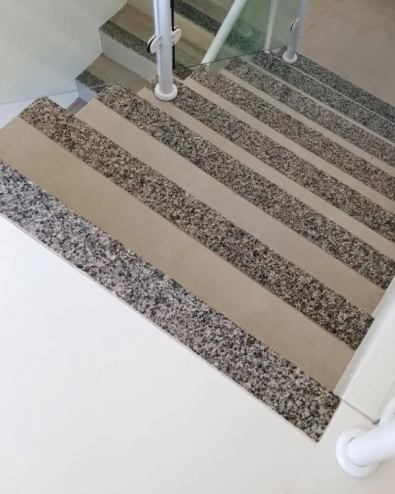 Escada com degraus revestidos em granito e piso claro, com guarda-corpo de vidro